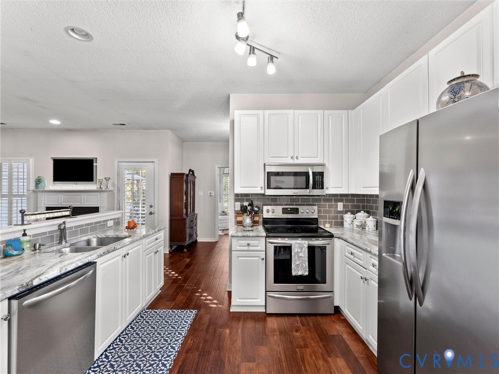 Kitchen featuring white cabinetry, stone-surface countertops, stainless steel appliances, a tile backsplash, and wood-finish flooring