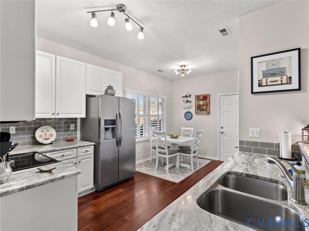 Kitchen featuring white cabinetry, stone-finish countertops, gray subway tile backsplash, dual-basin stainless steel sink, and wood-finish flooring