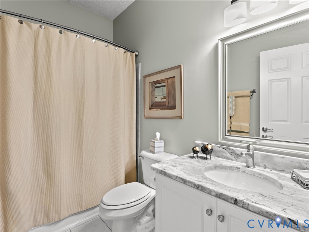 Bathroom vanity featuring stone-finish countertop, undermount sink, chrome-finish faucet, and white cabinetry, complemented by a large framed wall mirror and multi-bulb vanity light fixture