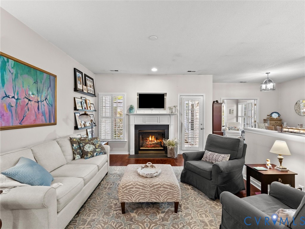 Living area featuring wood-finish flooring, a fireplace with a white mantel, and plantation shutters