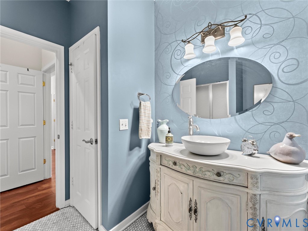 Bathroom vanity featuring a distressed white finish, countertop vessel sink, oval mirror, three-light fixture, and mosaic tile flooring