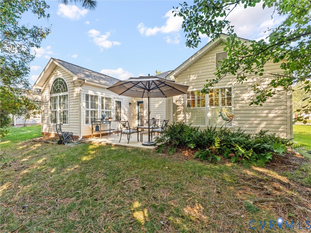 Exterior view featuring light-colored horizontal siding, arched window detailing, concrete patio, and mature landscaping