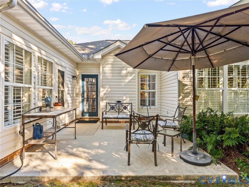 Concrete patio featuring light-colored horizontal siding, glass-paneled exterior door, and multi-pane windows
