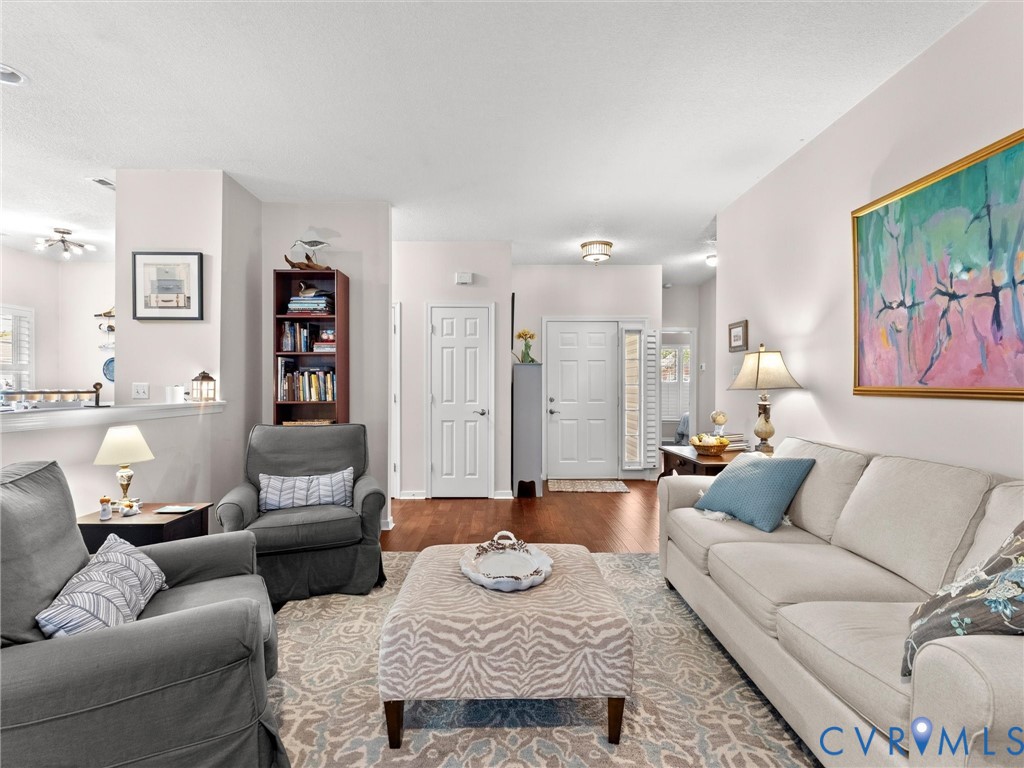 Open-concept living space featuring wood-finish flooring, neutral wall paint, a built-in recessed bookshelf, and a six-panel entry door with a side window light