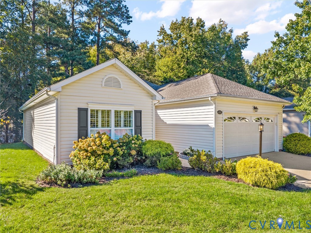 Vinyl-sided exterior featuring an attached two-car garage, manicured landscaping, arched window detailing, and a shingle roof