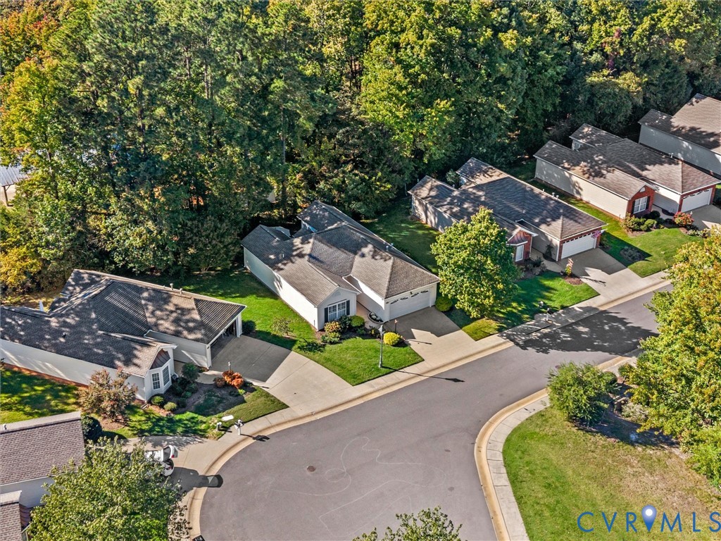 Aerial perspective of a single-story residence featuring a shingled roof, attached two-car garage, concrete driveway, and mature perimeter trees
