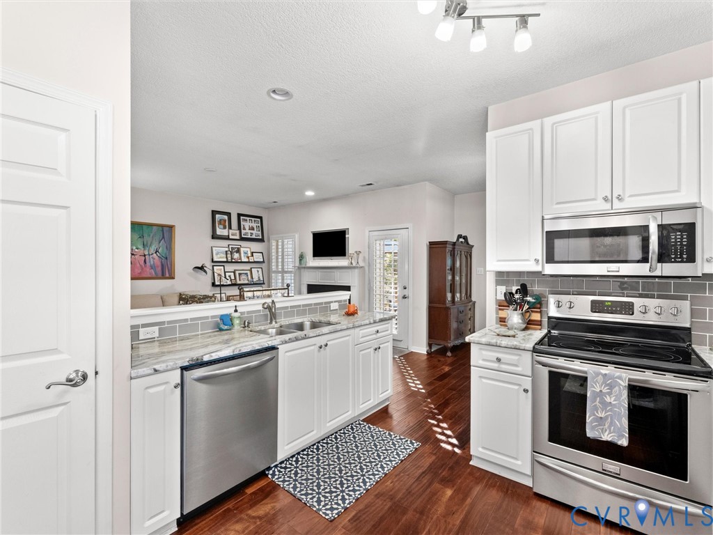 Kitchen featuring white cabinetry, stone-surface countertops, subway tile backsplash, stainless steel appliances, and wood-finish flooring