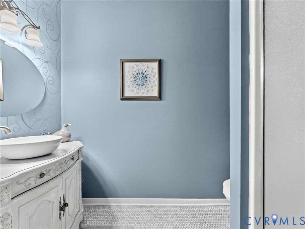 Vanity featuring a white cabinetry base with decorative detailing, a rounded vessel sink, and a multi-light wall fixture above an oval mirror