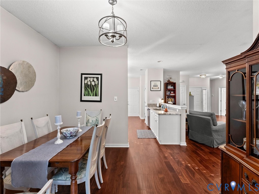 Wood-finish flooring, orb-style chandelier with three lights, and kitchen peninsula featuring a stone-look countertop