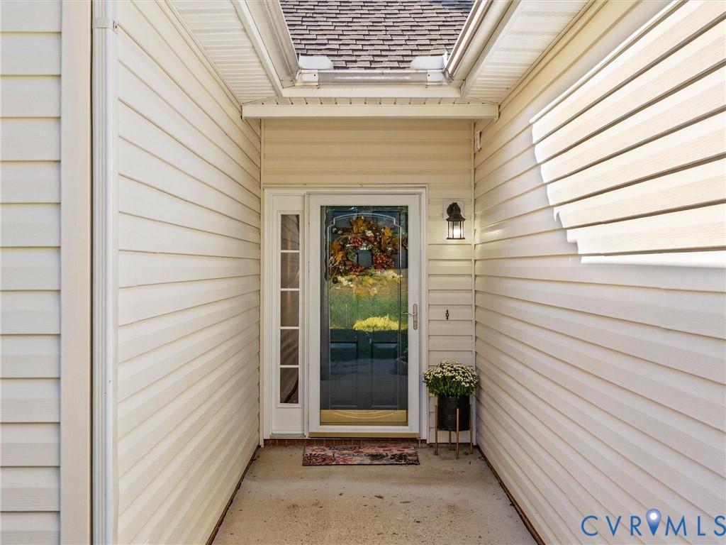Covered entryway featuring light-colored horizontal siding, a glass-panel door with sidelight, and an attached exterior wall-mounted light fixture