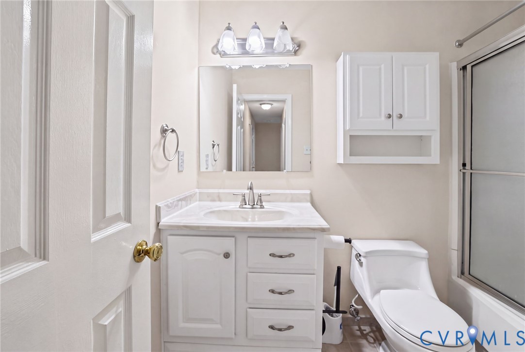 Bathroom featuring a white vanity cabinet with stone-look countertop, integrated sink, three-light fixture, wall-mounted storage cabinetry, and a shower enclosure