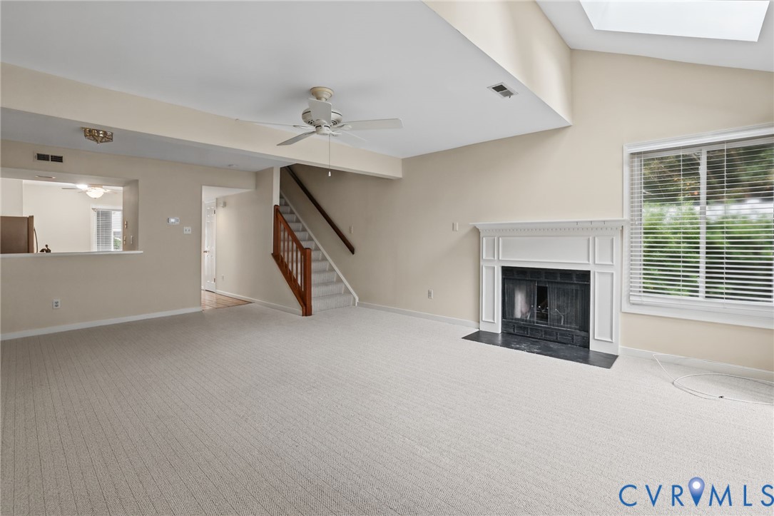 Vaulted ceiling featuring a skylight, fireplace with a decorative mantel and hearth, and a staircase with a wooden handrail