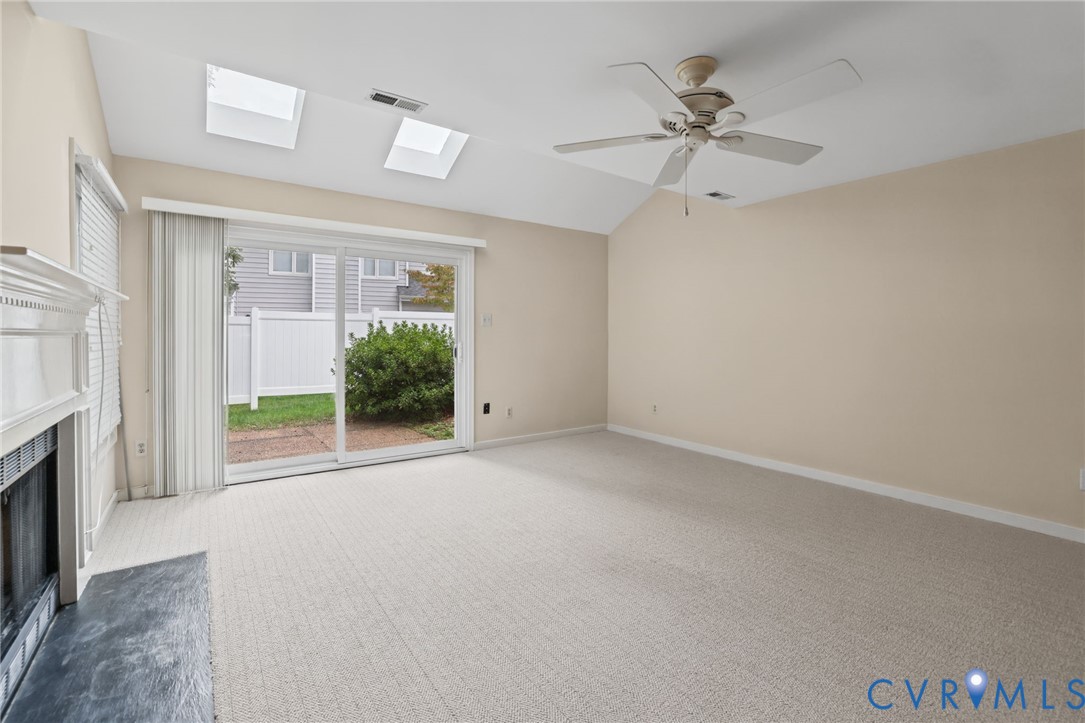 Vaulted ceiling room featuring dual skylights, a fireplace with a stone-finish hearth, a sliding glass door, and a ceiling fan