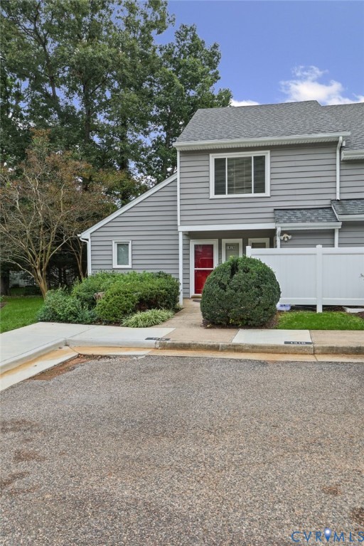 Two-story exterior featuring gray horizontal siding, asphalt shingle roofing, a concrete walkway, and a white privacy fence