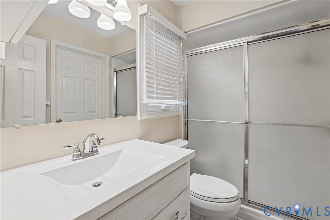 Bathroom featuring a white vanity with an integrated sink, polished chrome faucet, full-width mirror, and a walk-in shower with frosted sliding glass doors