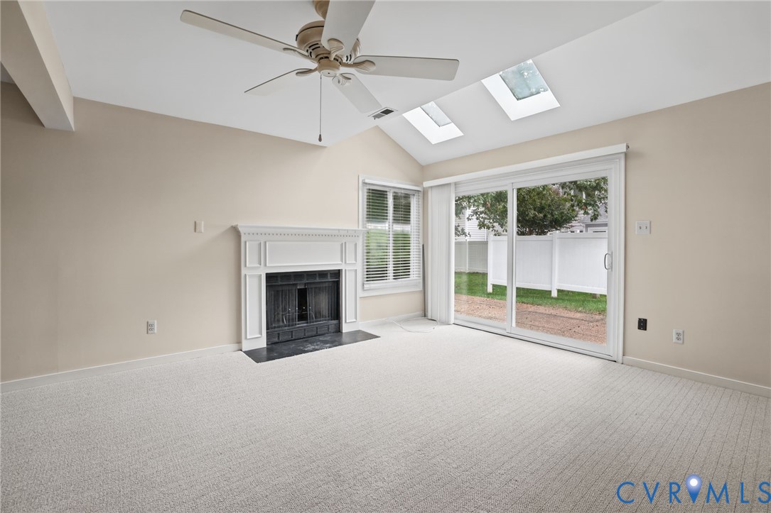 Living area featuring a fireplace with a white mantel, vaulted ceilings, dual skylights, a ceiling fan, and sliding glass doors