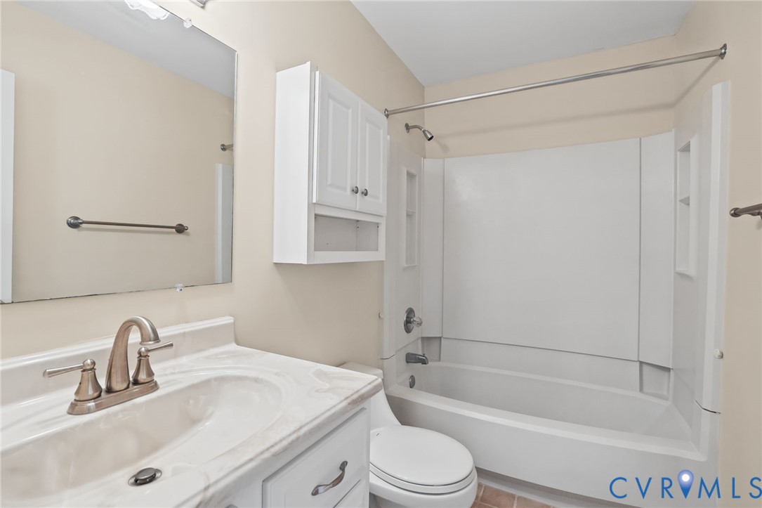 Bathroom featuring a white vanity with integrated sink, stone-composite countertop, wall-mounted storage cabinet, and a shower-tub combination with integrated shelving