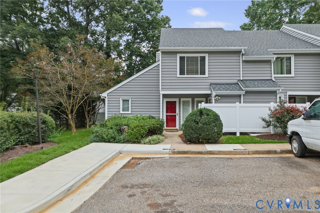 Grey horizontal siding exterior featuring a multi-gable roofline, a red front door, white privacy fencing, and concrete walkway