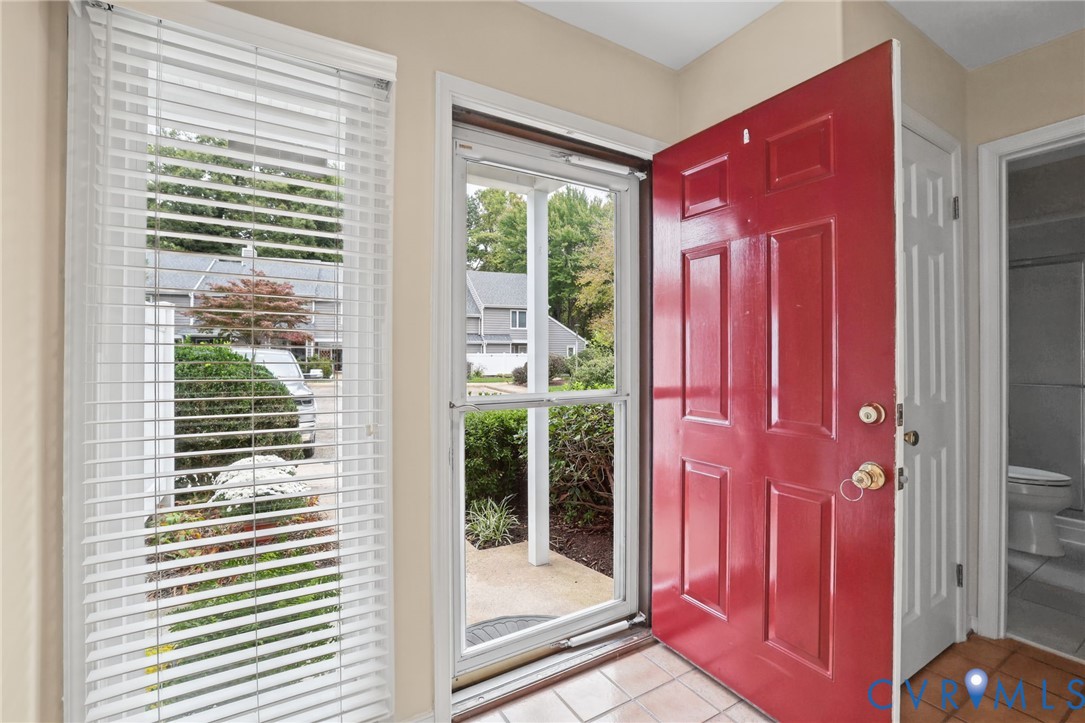 Entryway featuring a red six-panel front door, white storm door, window with horizontal blinds, and tile flooring