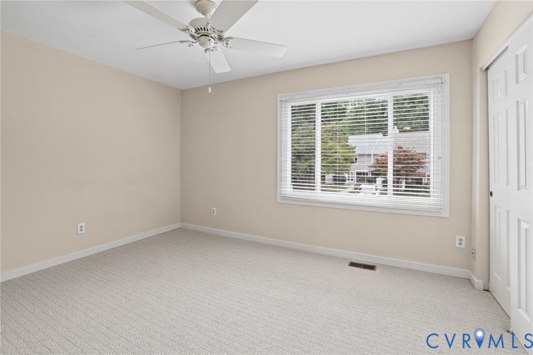 Neutral-toned interior featuring wall-to-wall carpeting, a multi-blade ceiling fan, and a large window with horizontal blinds