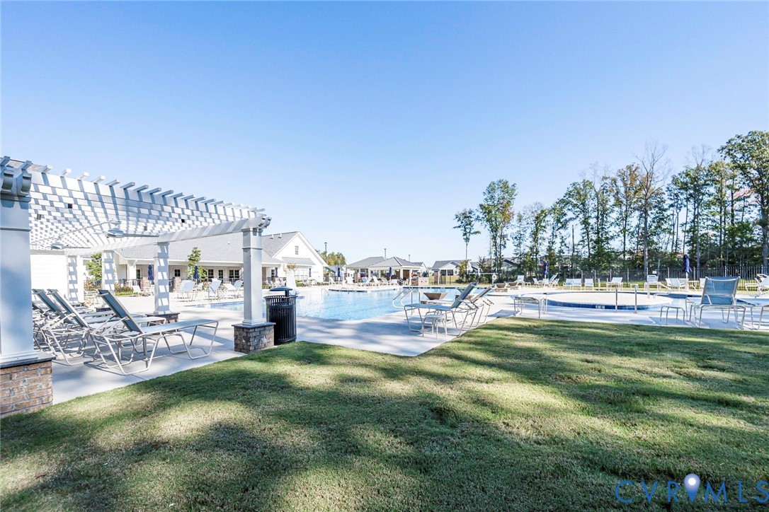 Swimming pool with concrete decking, pergola featuring stone-column bases, and a manicured lawn
