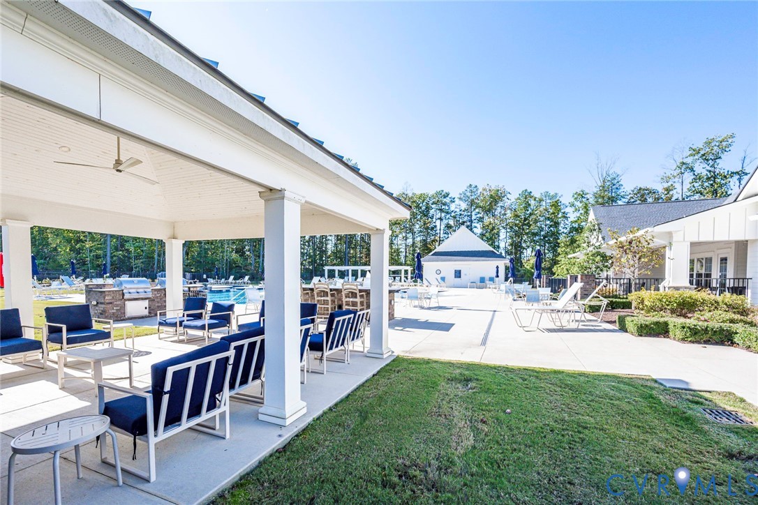 Covered outdoor pavilion featuring a vaulted beadboard ceiling, recessed lighting, and a ceiling fan, spanning a concrete patio area with a built-in stone-finished outdoor kitchen