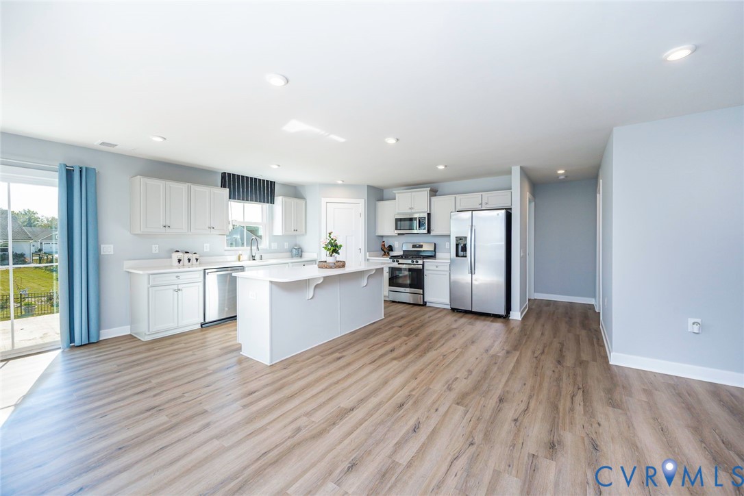 Kitchen Area with large central island with countertop seating, white shaker-style cabinetry, stainless steel appliances and walk in pantry