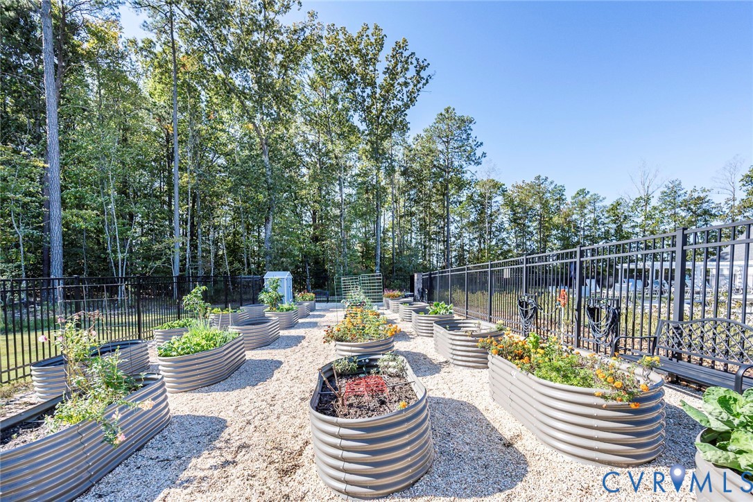 Garden area featuring multiple corrugated metal raised planting beds set within a gravel-surfaced space, enclosed by black metal fencing and bordered by mature trees