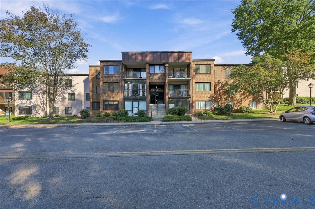 Multi-story brick exterior featuring recessed private balconies, copper-toned metal trim, and ground-level landscaping
