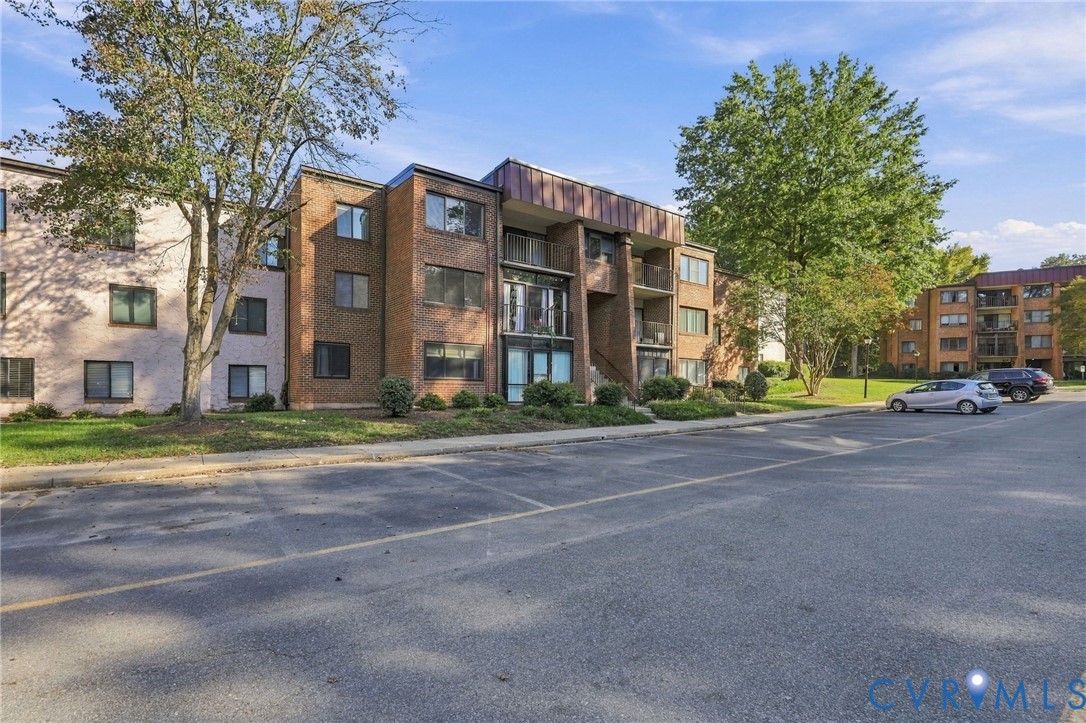 Multi-story brick exterior featuring recessed balconies, metal mansard roof detailing, and paved off-street parking