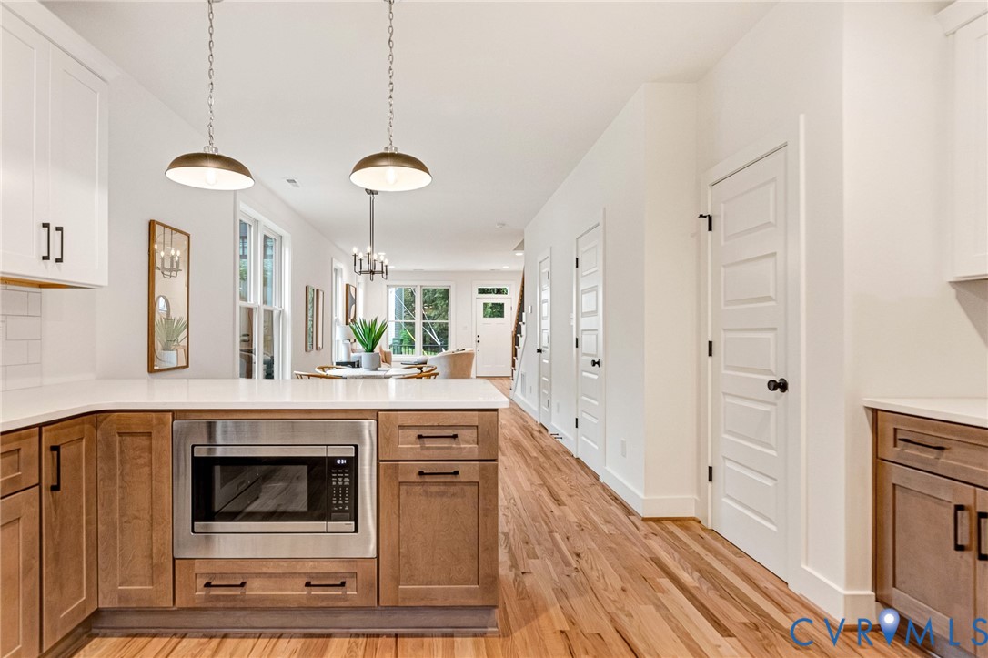 Kitchen featuring wood-finish cabinetry, white countertops, built-in stainless steel microwave, metal pendant lighting, and wood-finish flooring