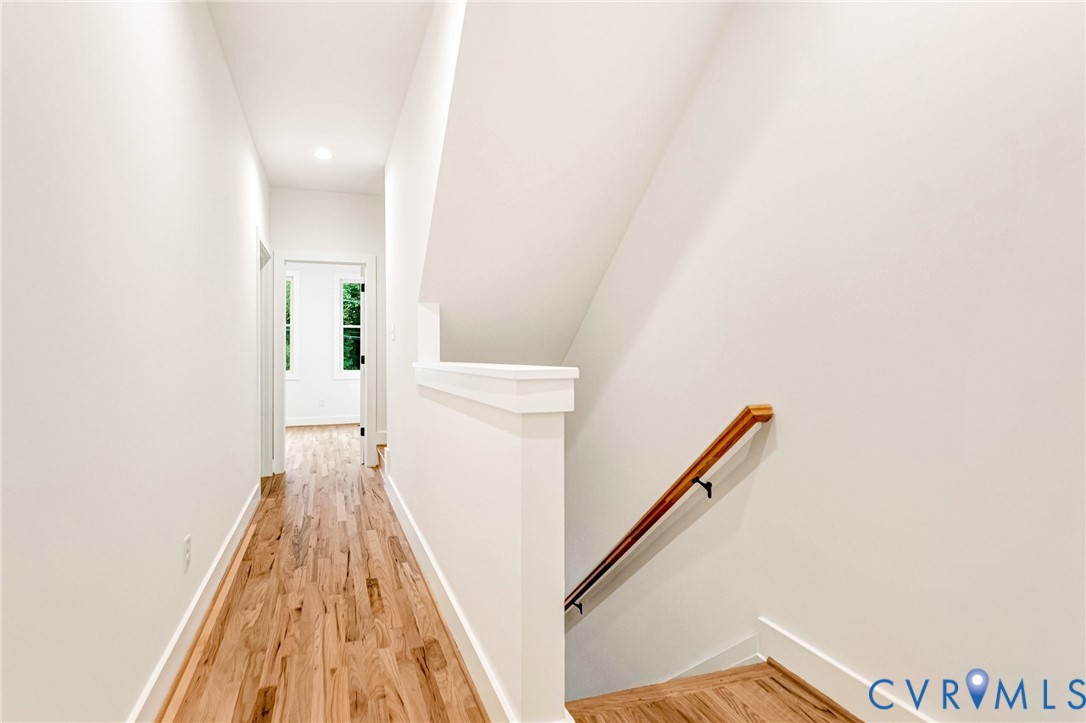 Hallway featuring wood-finish flooring, a wall-mounted wooden handrail, and recessed lighting
