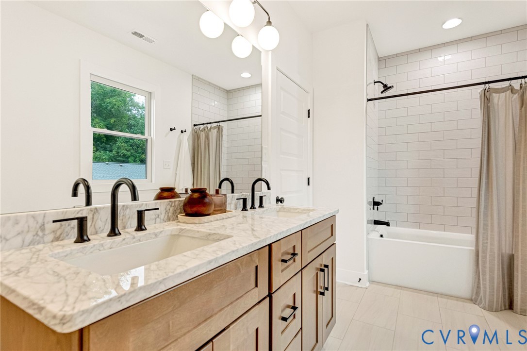 Bathroom featuring a dual-sink vanity with stone countertop, matte black fixtures, subway tile shower surround, and globe-style vanity lighting