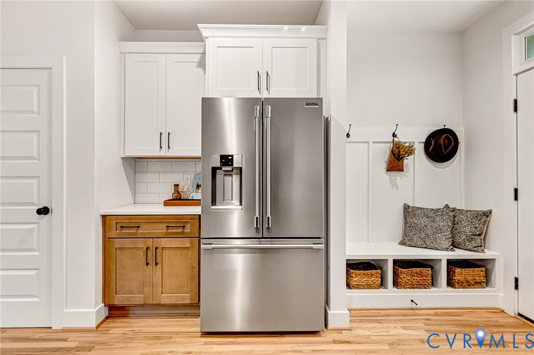 Custom cabinetry featuring a mix of painted white upper units and wood-finish lower cabinetry, white subway tile backsplash, built-in mudroom bench with cubby storage, stainless steel French door refrigerator, and white board-and-batten wall detailing