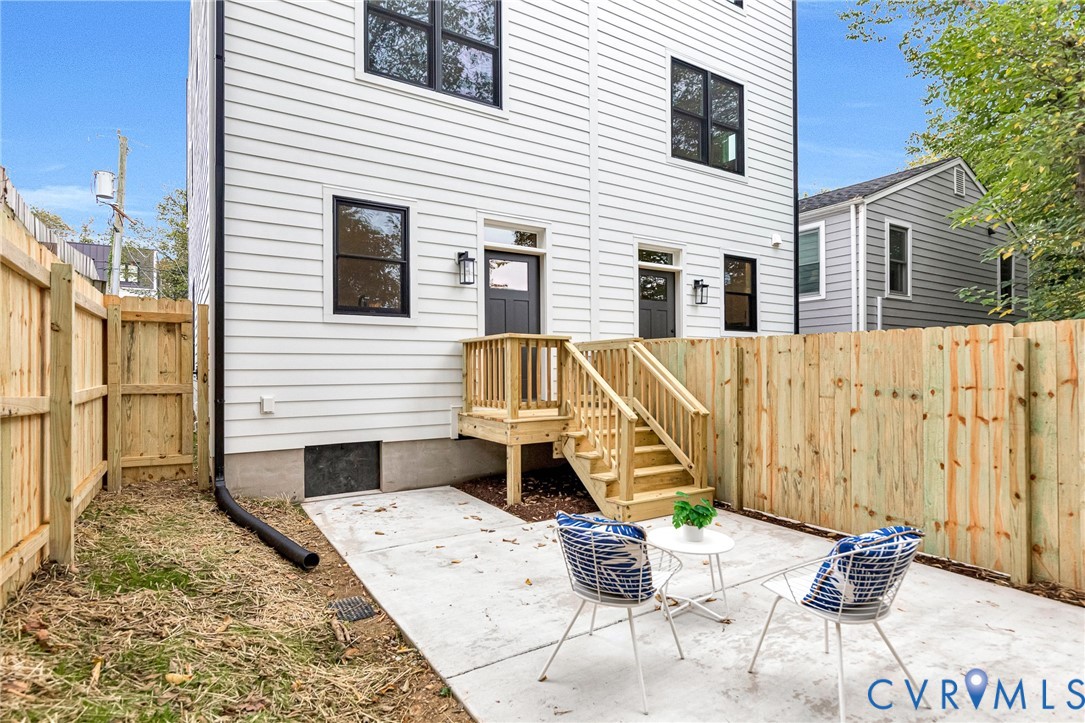 White horizontal siding exterior featuring black-framed windows, a concrete patio, wood-railing stairs, and a full-height privacy fence