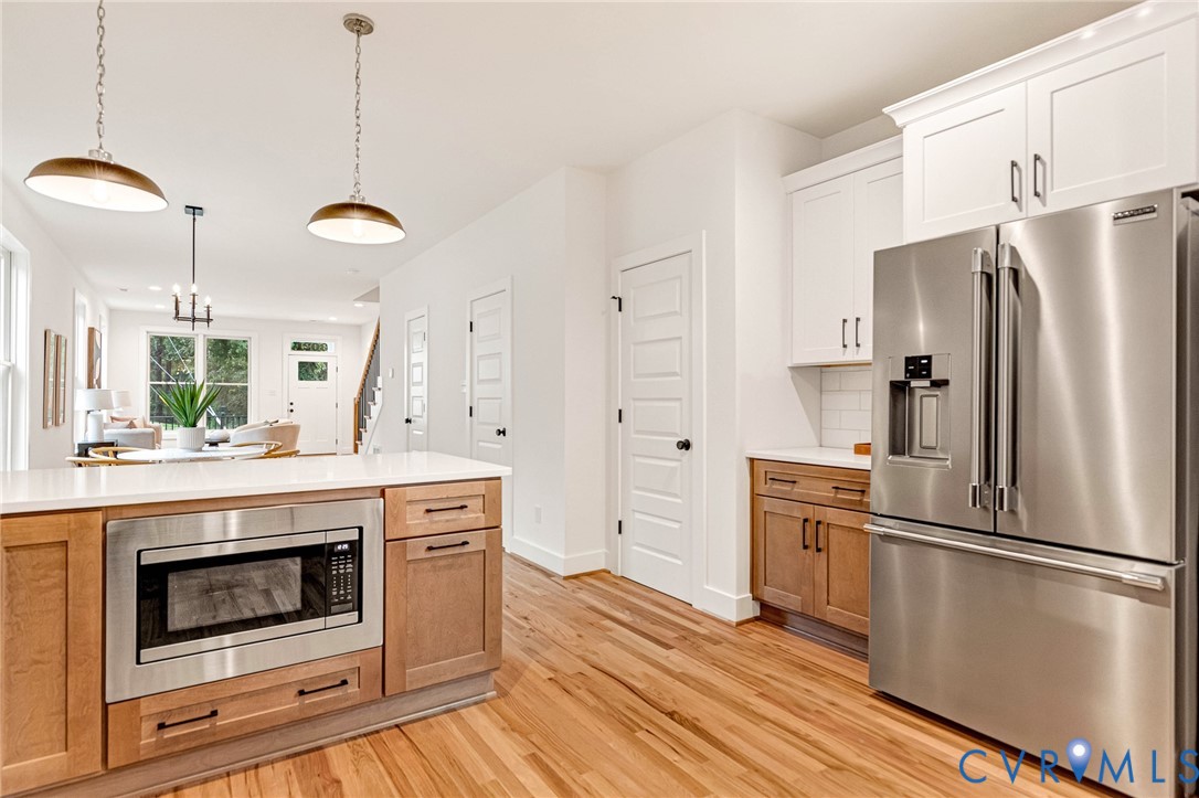 Kitchen featuring two-tone cabinetry, stainless steel appliances, quartz countertops, wood-finish flooring, and pendant lighting