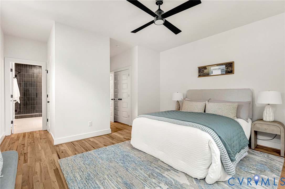 Wood-finish flooring, multi-panel doors with matte black hardware, matte black ceiling fan, and walk-in shower with vertical tile surround