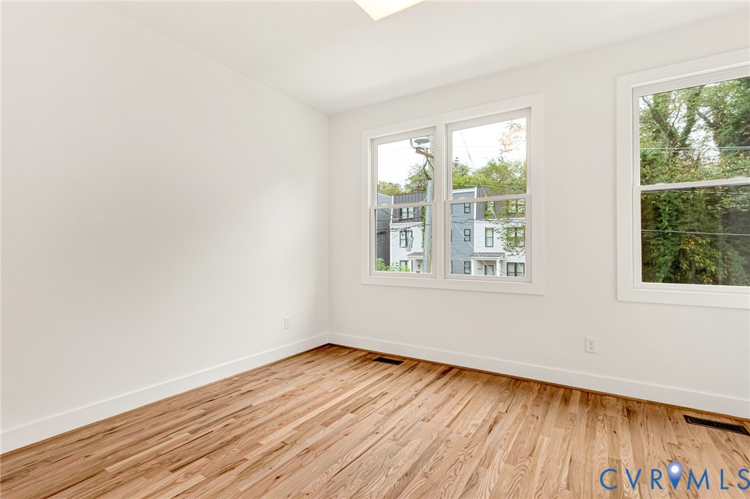 Bright interior space featuring wood-finish flooring, crisp white walls, and dual-pane windows with exterior greenery