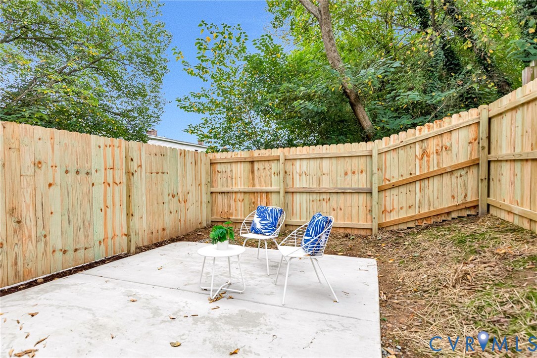 Concrete patio enclosed by a wood privacy fence with surrounding mature trees