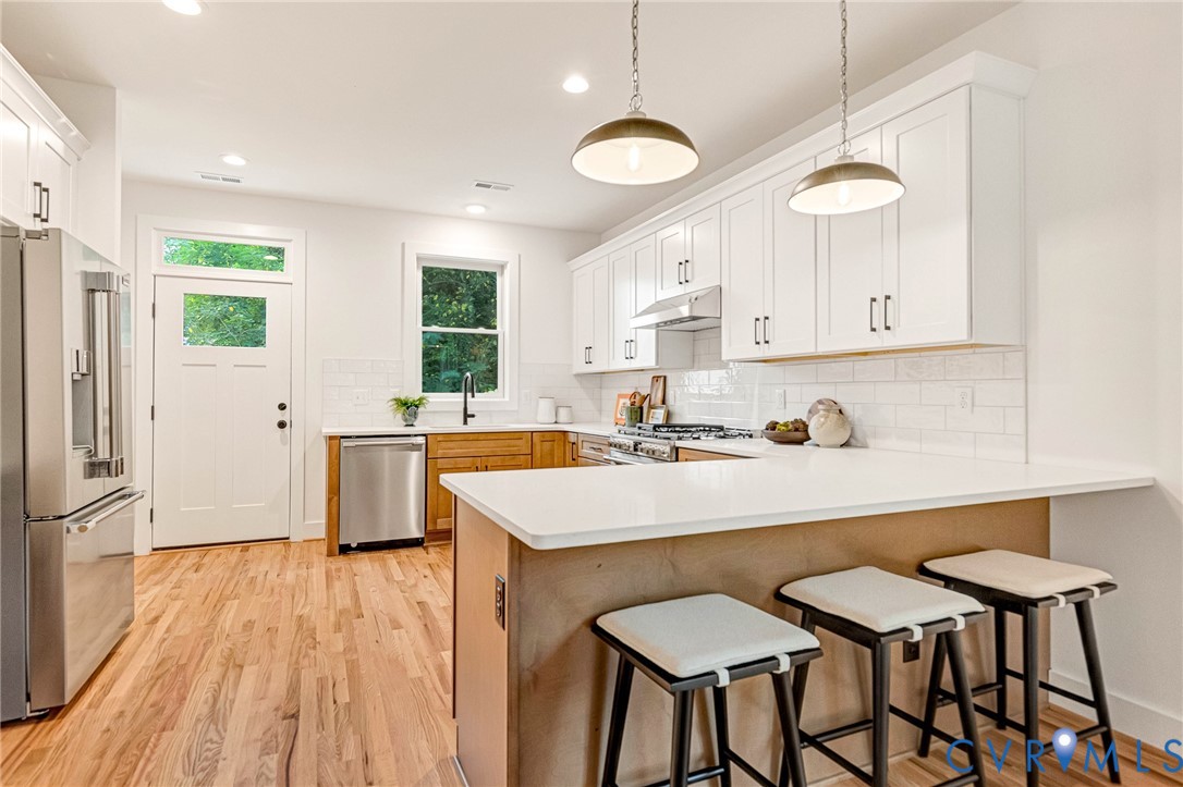 Kitchen featuring white shaker-style cabinetry, solid-surface countertops, subway tile backsplash, stainless steel appliances, and wood-finish flooring