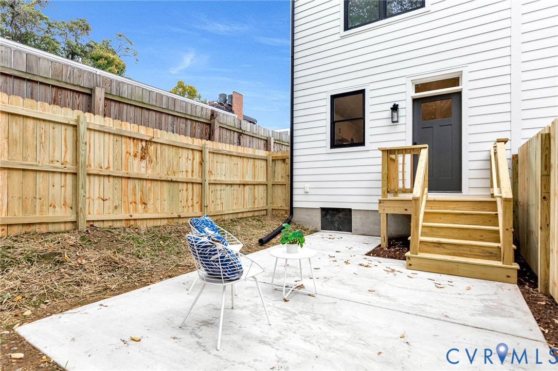 Exterior patio featuring a concrete slab, wood privacy fencing, and a built-in wood staircase with railing leading to a dark-finished entry door