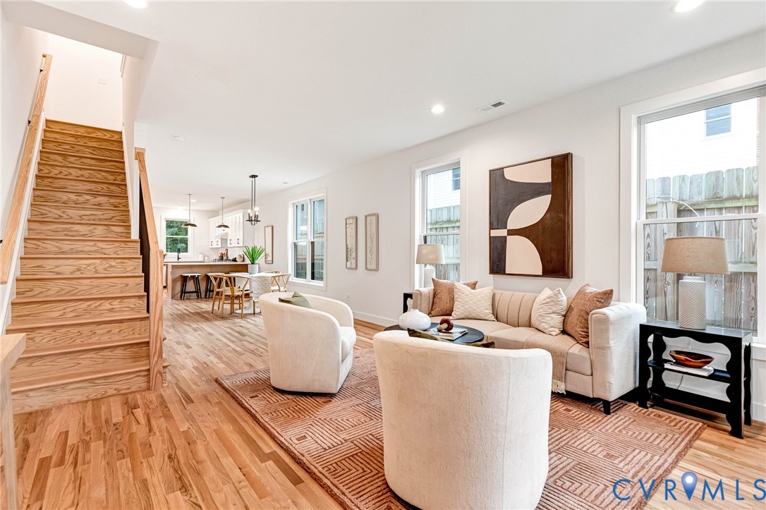 Open-concept interior featuring wood-finish flooring, staircase with wood treads, recessed lighting, and multiple windows