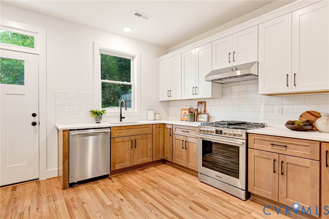 Kitchen featuring white upper cabinets, wood-finish lower cabinetry, stone-style countertops, white subway tile backsplash, and stainless steel appliances