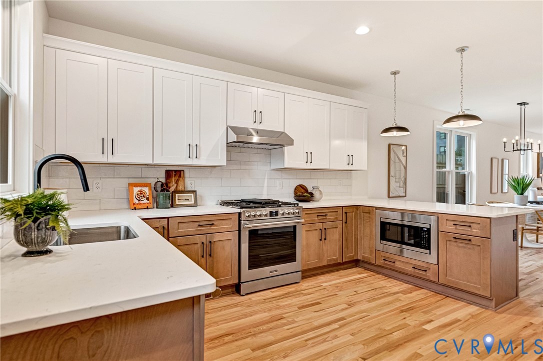 Kitchen featuring white upper cabinetry, light wood-finish base cabinetry, quartz countertops, white tile backsplash, and stainless steel appliances