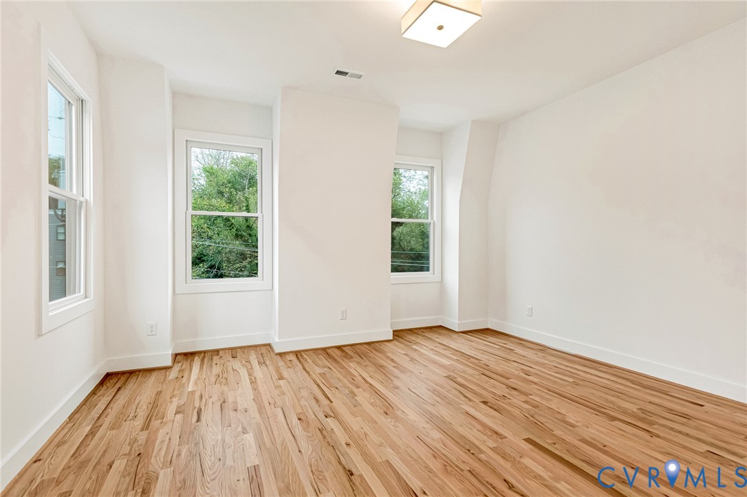 Interior space featuring wood-finish flooring, three double-hung windows, and a flush-mount light fixture