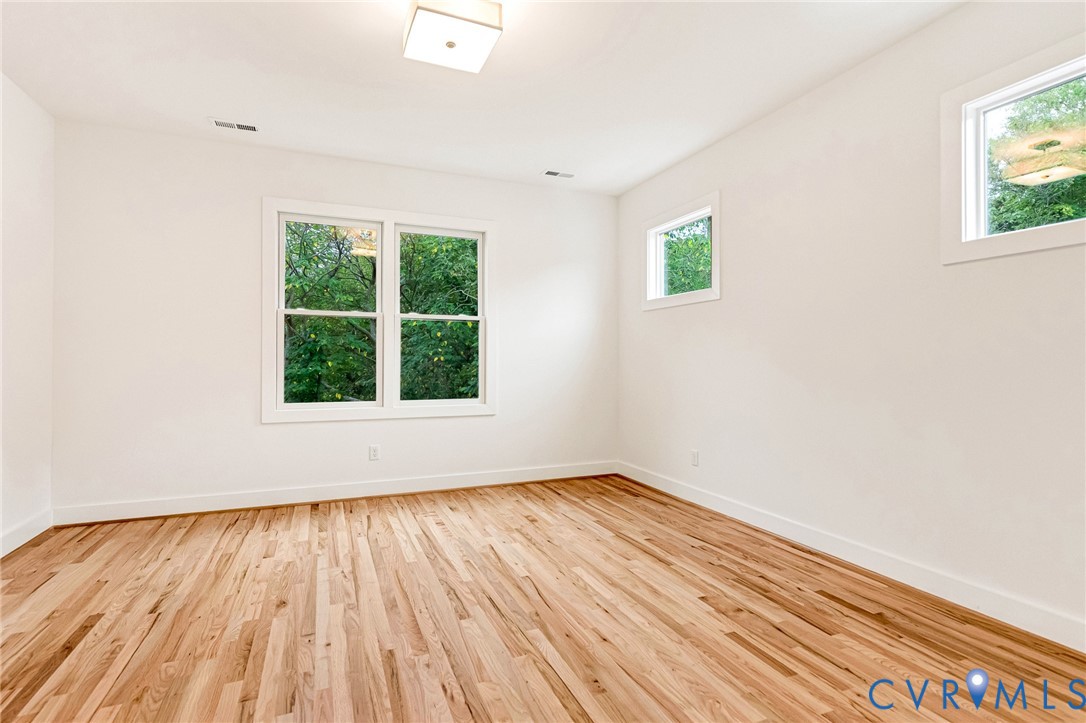 Bright room featuring wood-finish flooring, white walls, double-pane windows, and a flush-mount ceiling light fixture
