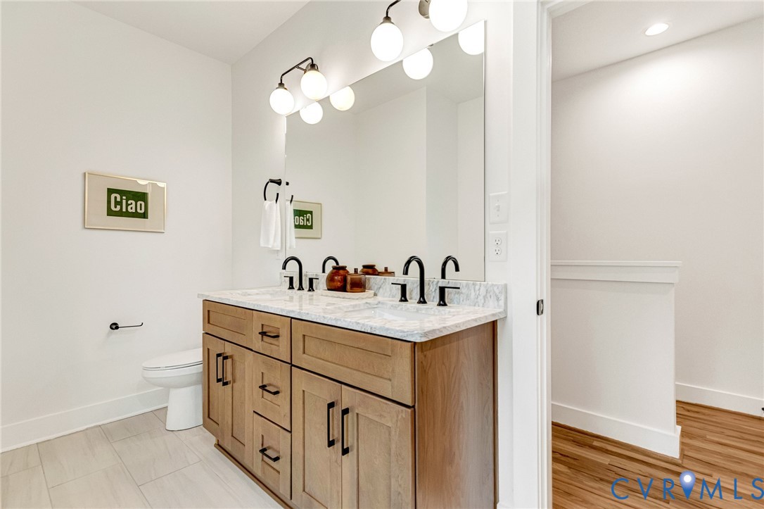 Double vanity featuring wood-finish cabinetry, stone-patterned countertop, dual undermount sinks, matte black fixtures, and a large wall-mounted mirror