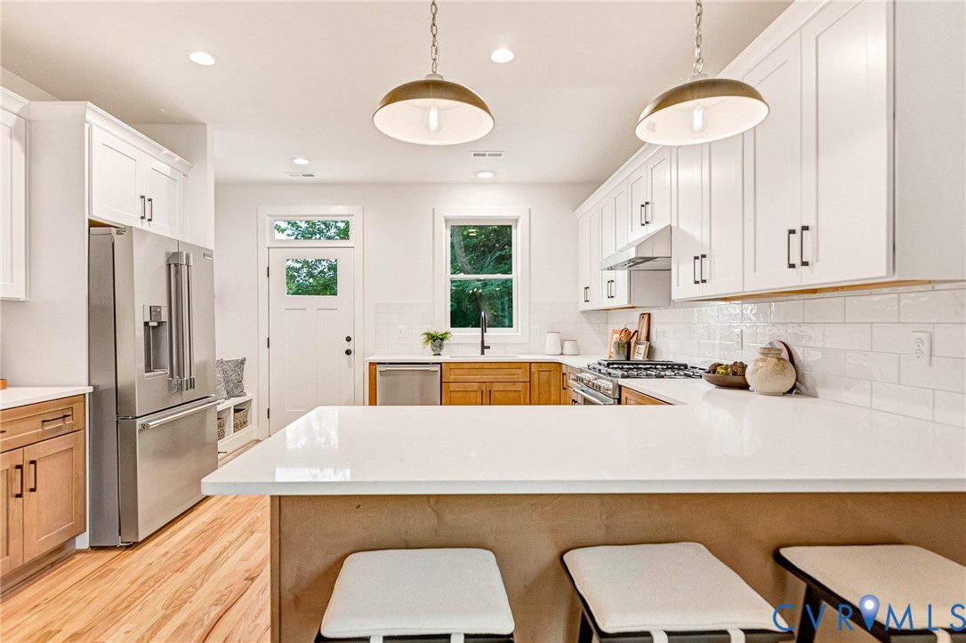 Kitchen featuring white shaker-style cabinetry, a quartz countertop island, stainless steel appliances, a white subway tile backsplash, and light wood-finish flooring