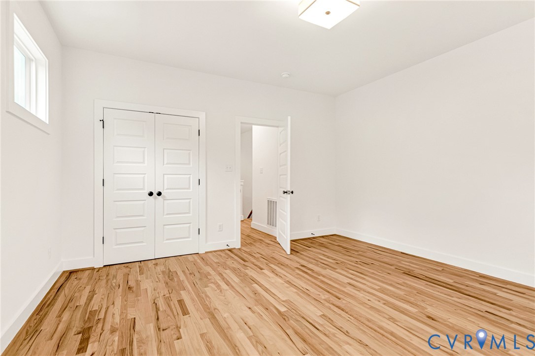 Interior room featuring wood-finish flooring, white walls, double doors with matte black hardware, and a square flush-mount ceiling light fixture