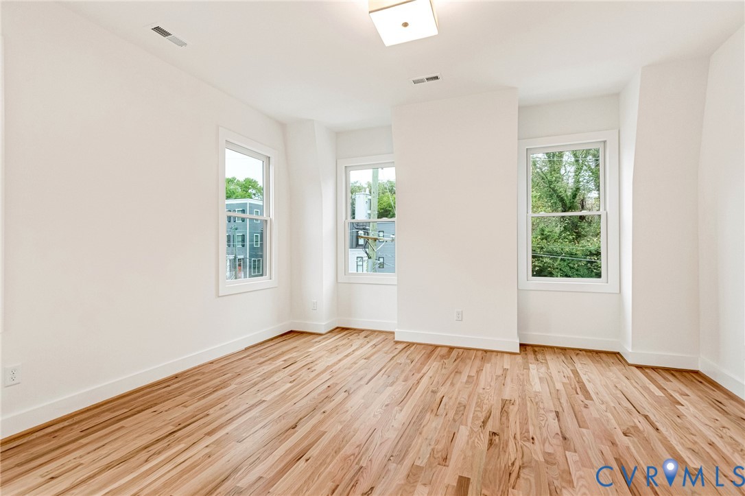 Interior space featuring wood-finish flooring, white walls, three double-hung windows, and a flush-mount light fixture